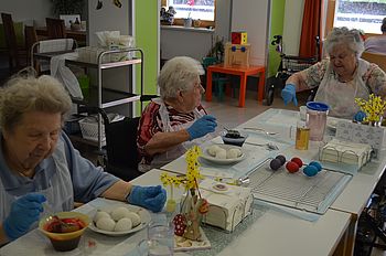 drei Bewohnerinnen sitzen beim Tisch und färben die Eier