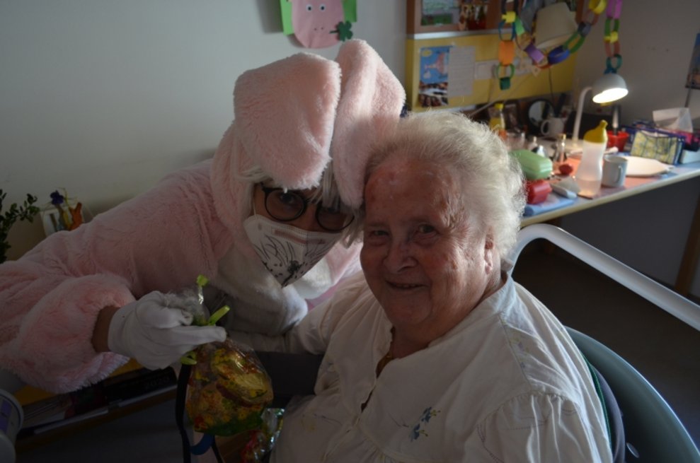 Eine Person, die als Osterhase verkleidet ist, steht neben einer Bewohnerin.