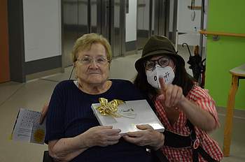 Eine Betreuerin sitzt neben einer Bewohnerin, die eine Schachtel Pralinen in der Hand hält.