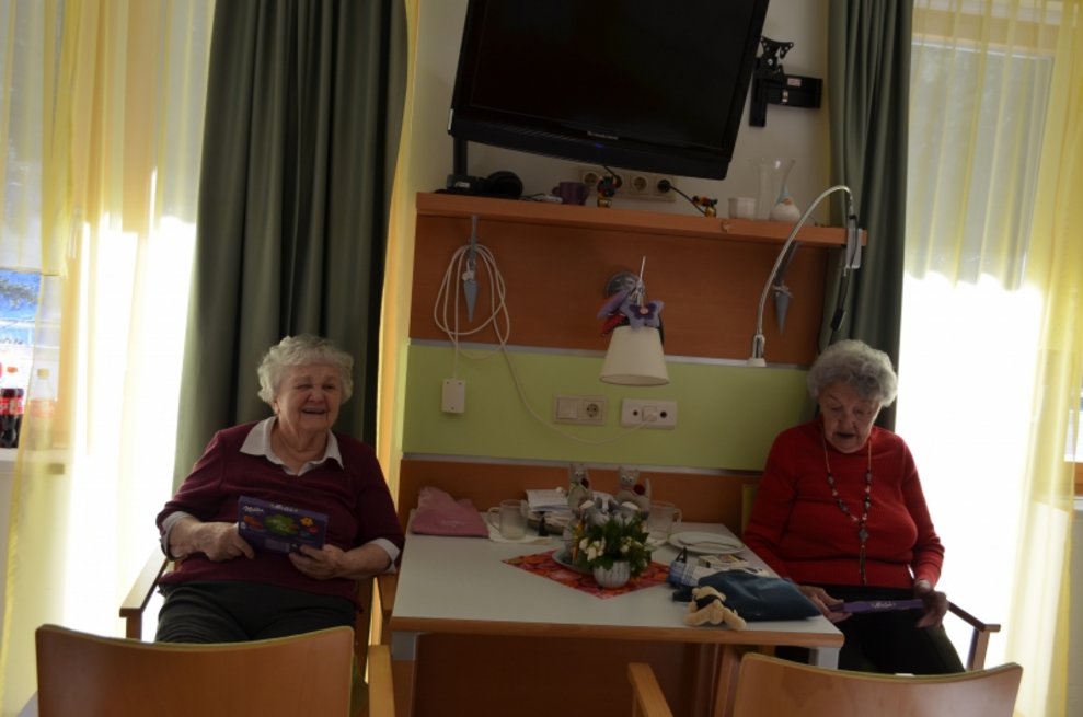 Zwei Bewohnerinnen sitzen nebeneinander und halten Schokolade.