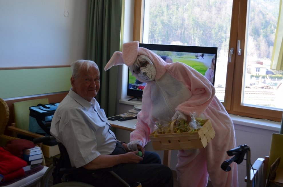Eine Person, die als Osterhase verkleidet ist, gibt einem Bewohner einen Geschenkkorb.