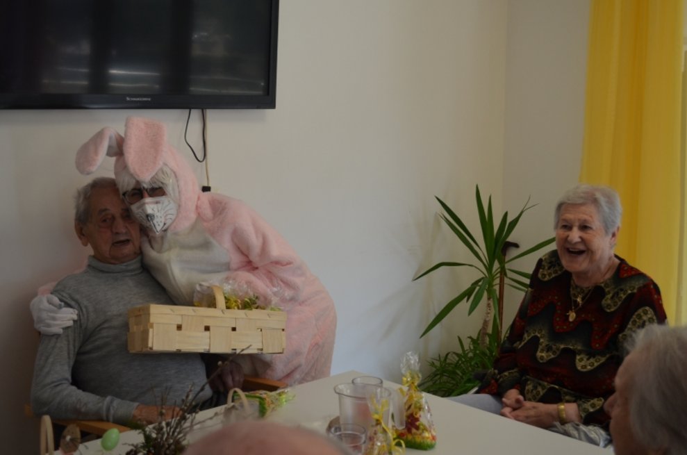 Eine Person, die als Osterhase verkleidet ist, umarmt einen Bewohner.